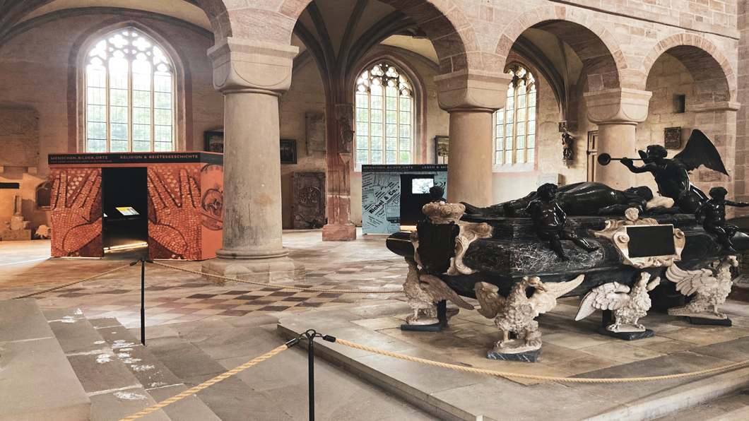 Ein roter und ein orangener Ausstellungskubus sind in dem Innenraum des Münsters in Heilsbronn platziert. 