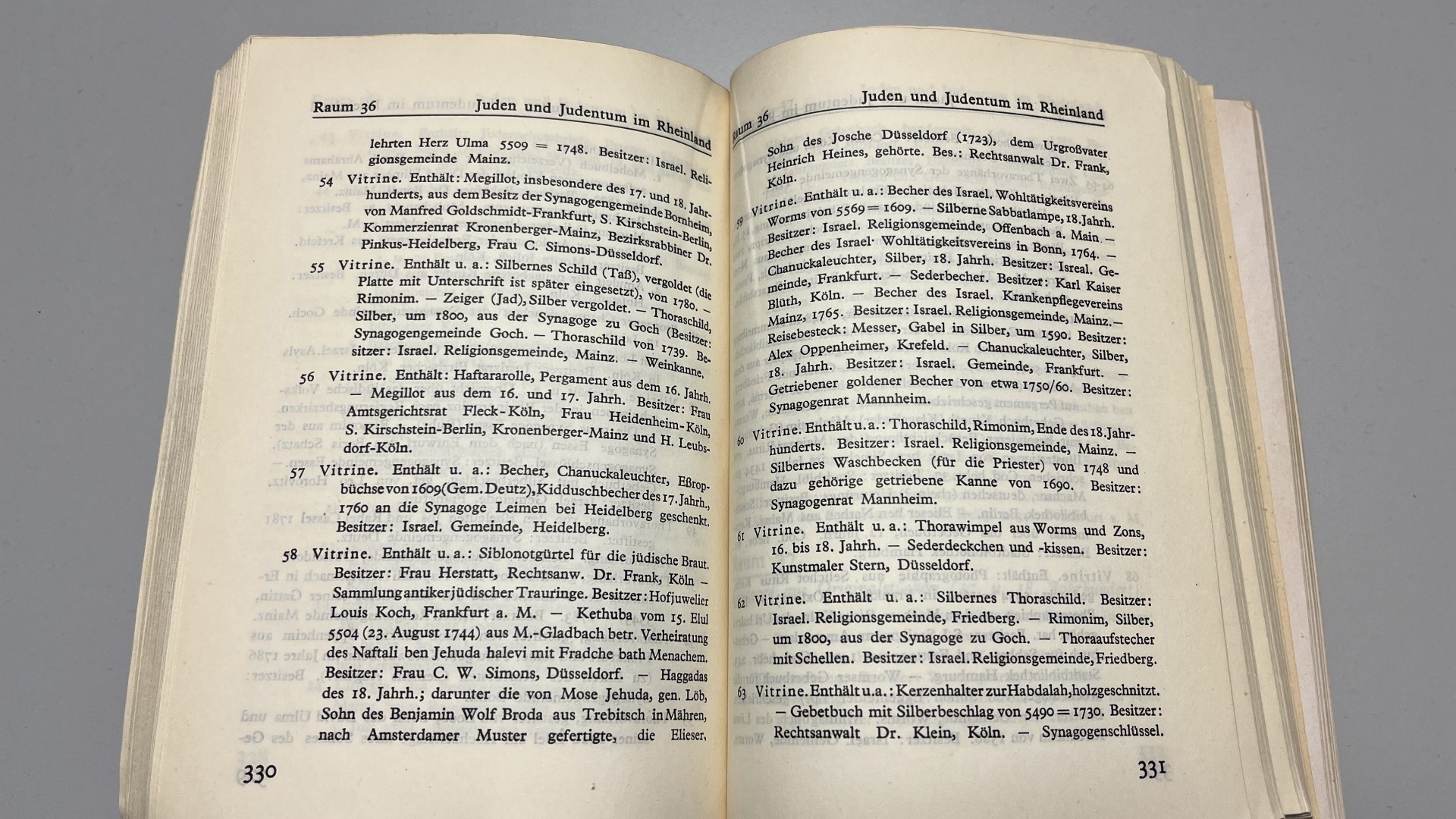 Nahaufnahme des Ausstellungskatalogs der Jahrtausend-Ausstellung, der aufgeschlagen auf einem Tisch liegt. Das Kapitel "Juden und Judentum in Rheinland" ist aufgeschlagen und zeigt eine Auflistung der Vitrinen mit Judaika-Objekten.