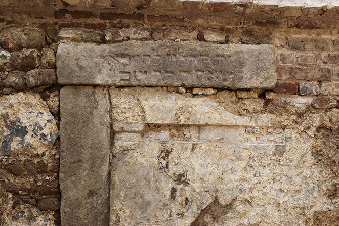 Nahaufnahme einer Inschrift mit hebräischen Schriftzügen, die in der mittelalterlichen Mauer eines Kellers im unterirdischen Rundgang von MiQua reingeritzt sind.