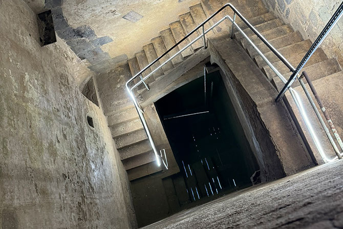 Von oben blickt man tief runter in den Schacht der Kölner Mikwe. Die Wände sind aus hellem Stein. Tief unten kann man das mit Wasser gefüllte Tauchbecken sehen.