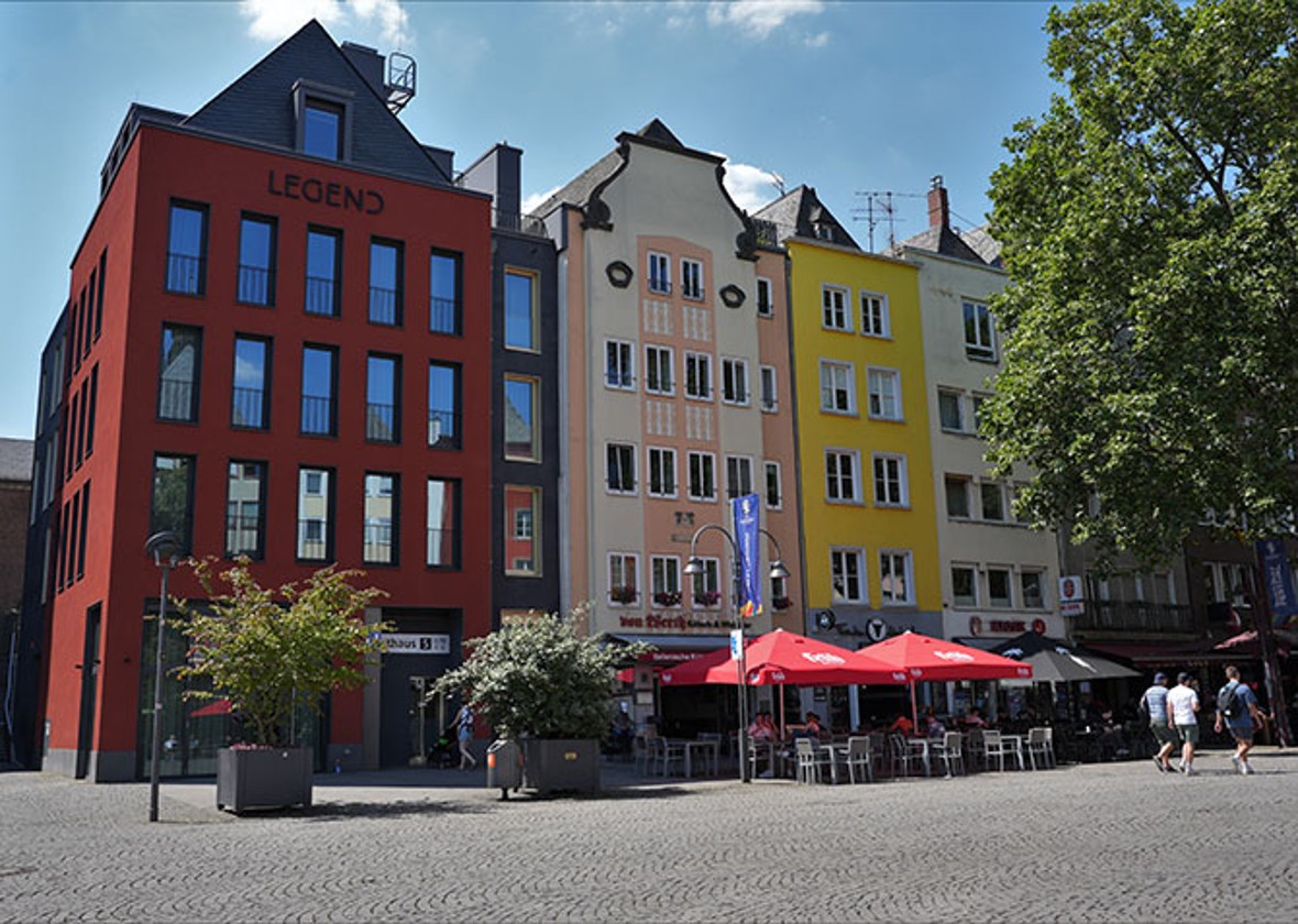 Der Alter Markt in Köln mit dem roten Haus. Im Erdgeschoss des Roten Haus am Alter Markt befindet sich das MiQua:forum. Links neben dem Roten Haus befindet sich der Rathausturm. Rechts neben dem Haus befinden sich weitere, schmale Häuser.