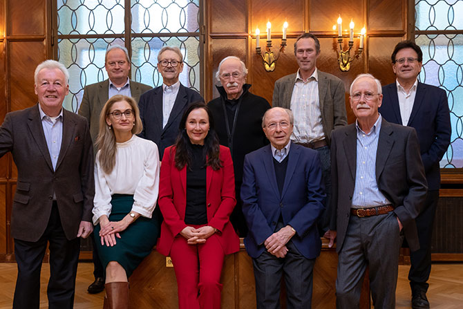 Gruppenfoto des Vorstands der Fördergesellschaft MiQua-Freunde. Acht Männer und zwei Frauen sitzen und stehen für das Gruppenfoto dicht beieinander. Die hintere Reihe steht, die vordere Reihe sitzt. Im Hintergrund leuchtet warmes Licht.