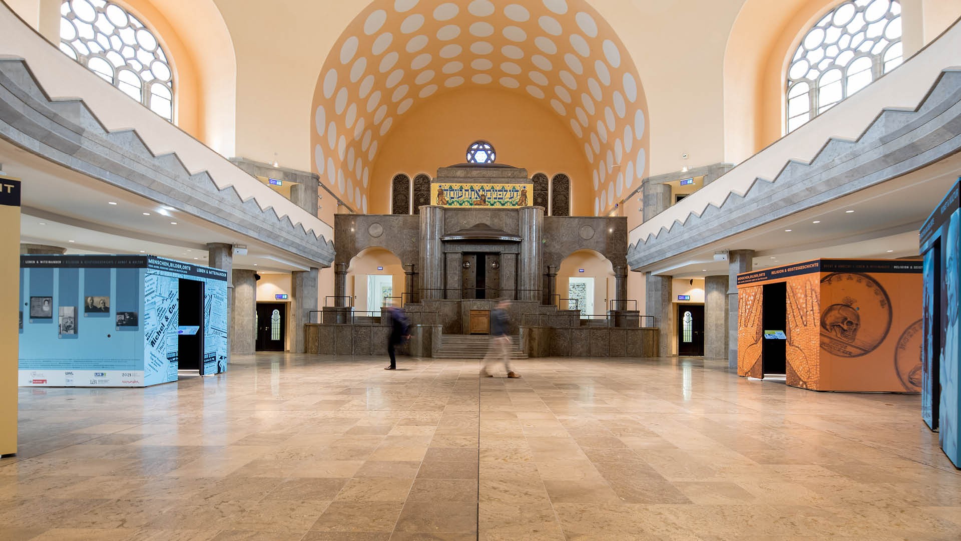 Eine große, helle Ausstellungshalle.  Hier sind die begehbaren Kuben der Ausstellung "Menschen, Bilder, Orte – 1700 Jahre jüdisches Leben in Deutschland" zu sehen.