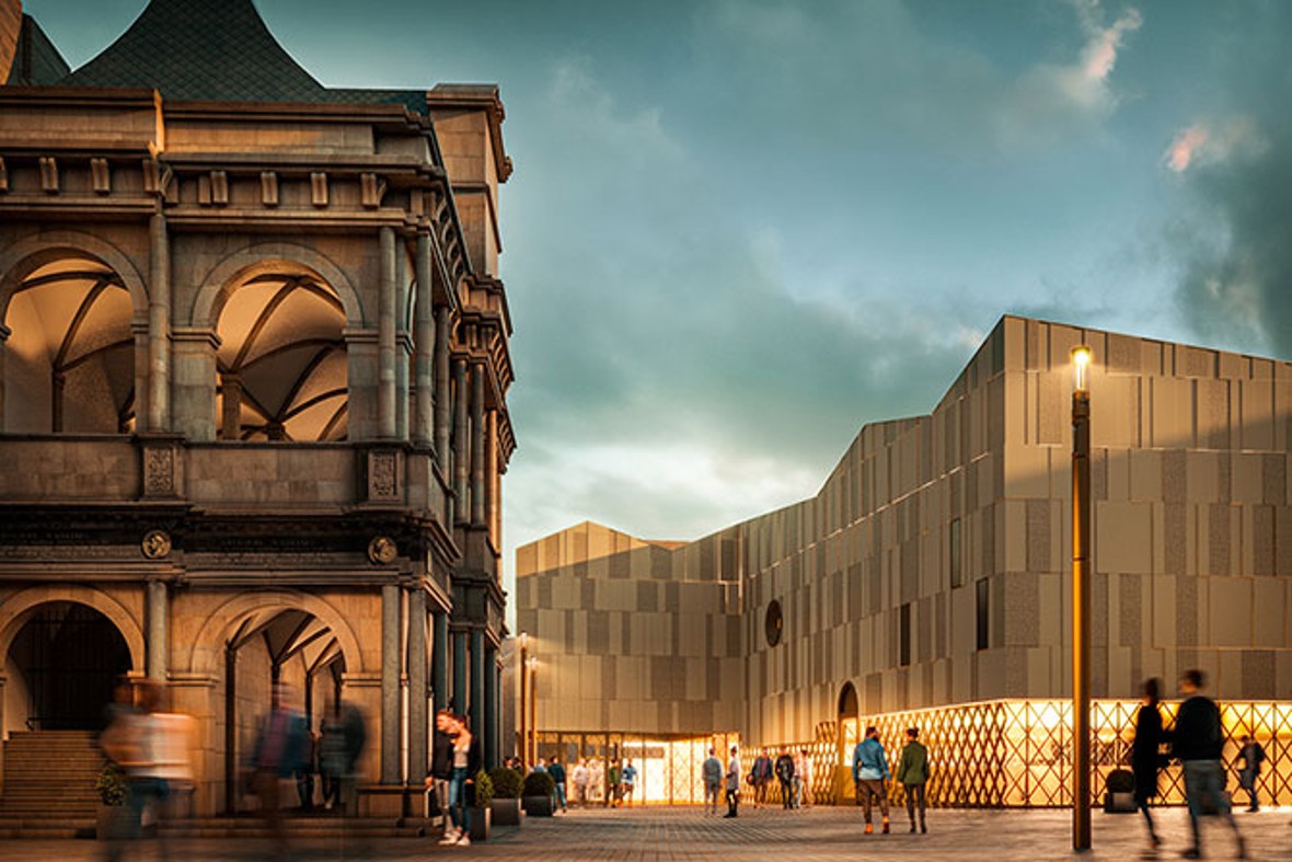 Fußgänger spazieren über den Rathausplatz mit dem abendlich erleuchtete Museumsgebäude auf der rechten Seite und links die historische Renaissancelaube des Rathauses.