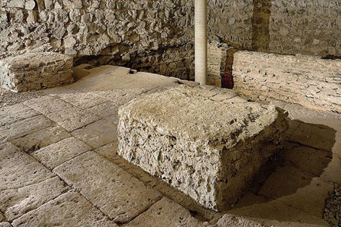 Ein Boden aus sandfarbenen, großen Steinblöcken. Eine Steinblock ist rechts auf dem Boden zu sehen. Im Hintergrund ist eine sandfarbige Steinwand zu sehen. 