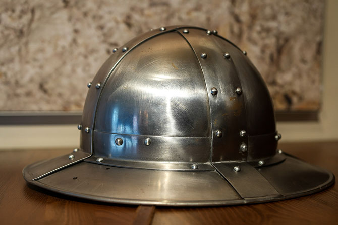 Ein Helm aus silbernen Metall liegt vor einem Hintergrund einer Steinmauer.