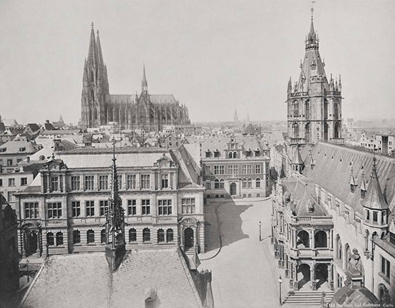 Ein historisches Foto in schwarz-weiß. Im Vordergrund sieht man mehrere Mehrfamilienhäuser und Bürogebäude. Im Hintergrund sieht man eine Kathedrale, rechts einen Turm, der einem Kirchengebäude ähnelt.