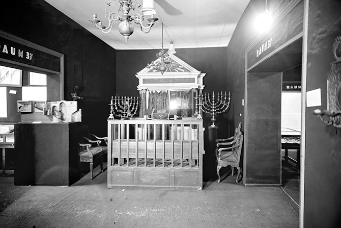 Ein schwarz-weiß Foto das einen Ausstellungsraum mit jüdischen Gegenständen zeigt.