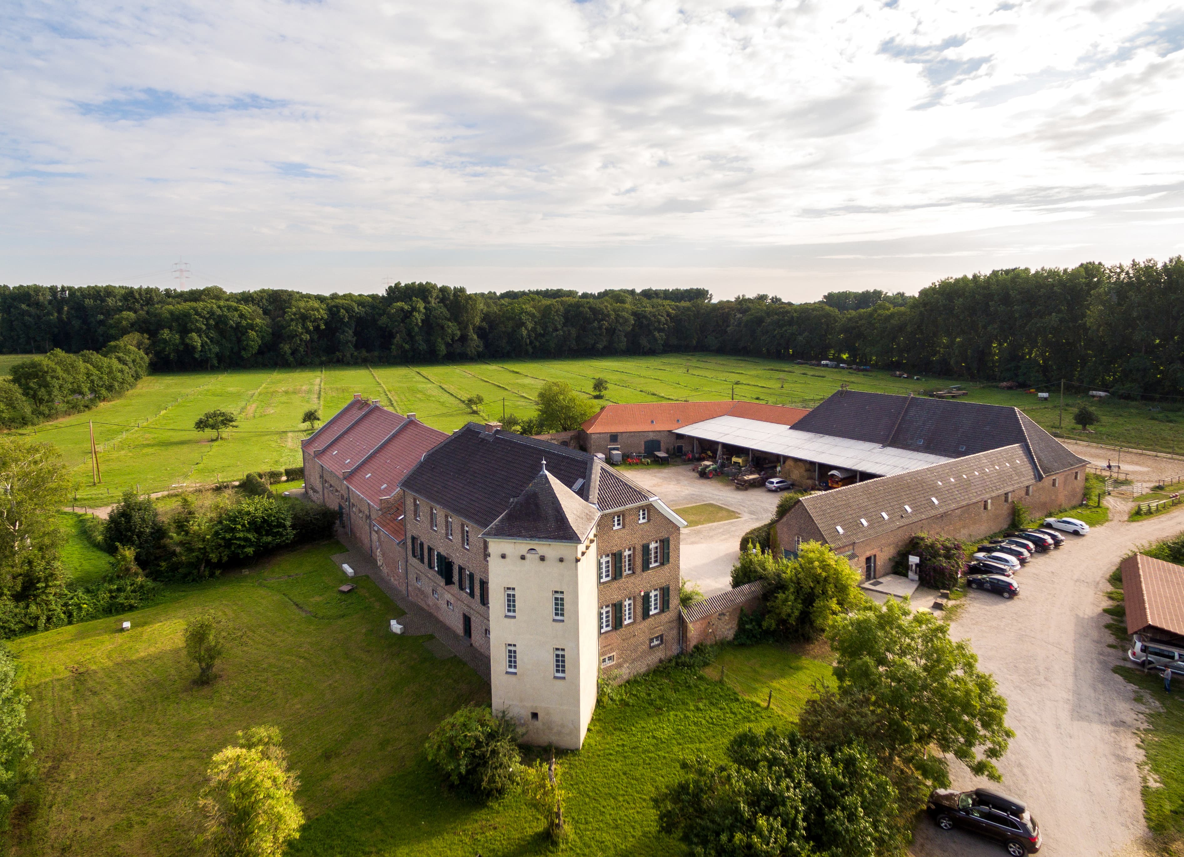 Luftaufnahme eines quadratischen Gutshofs mit einem Turm der in grüner Umgebung liegt.
