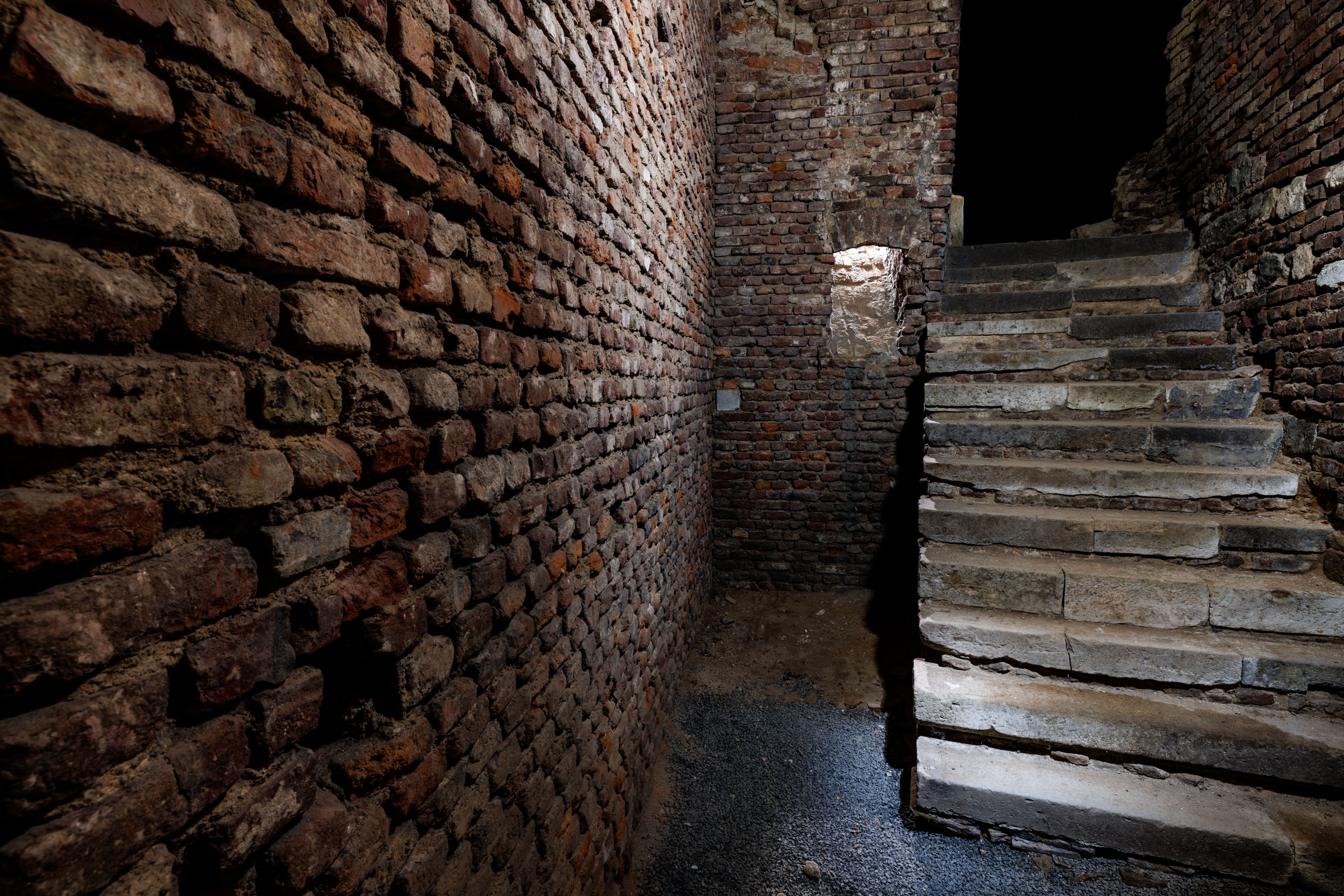 Eine Treppe aus weißem und grauen, glatten Stein. Links eine Wand aus dunkelbraun-rötlichen Steinen.