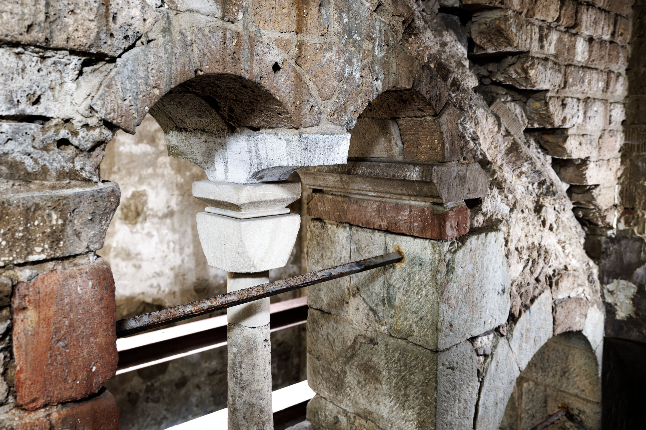 Altes, grau-beiges Gemäuer in Form eines schmalen Torbogens, der in der Mitte durch eine weiße Säule gestützt wird.
