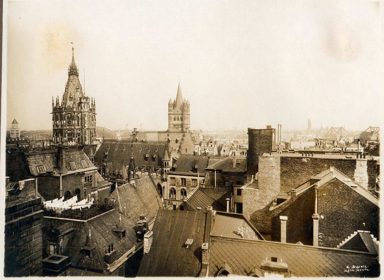 Ein schwarz-weiß Foto einer Skyline. Viele Dächer und zwei Kirchtürme sind zu sehen.