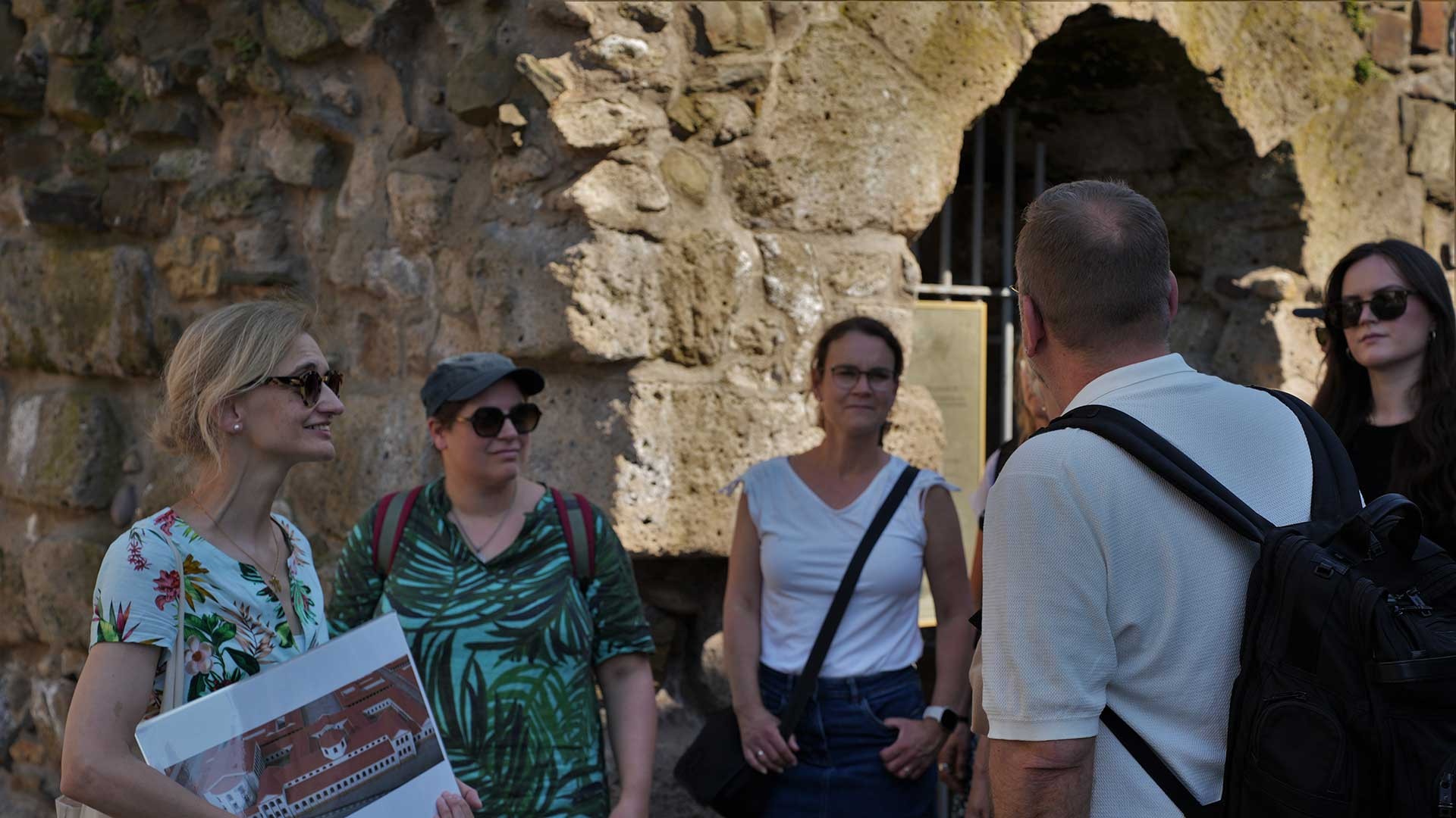 Eine Gruppe von Menschen steht vor dem Eingang zum römischen Abwasserkanal während einer Führung.  